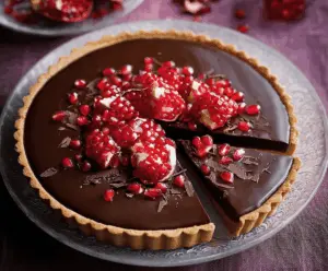 Delicious Chocolate Pomegranate Tart topped with fresh pomegranate seeds and rich chocolate ganache on a decorative plate.