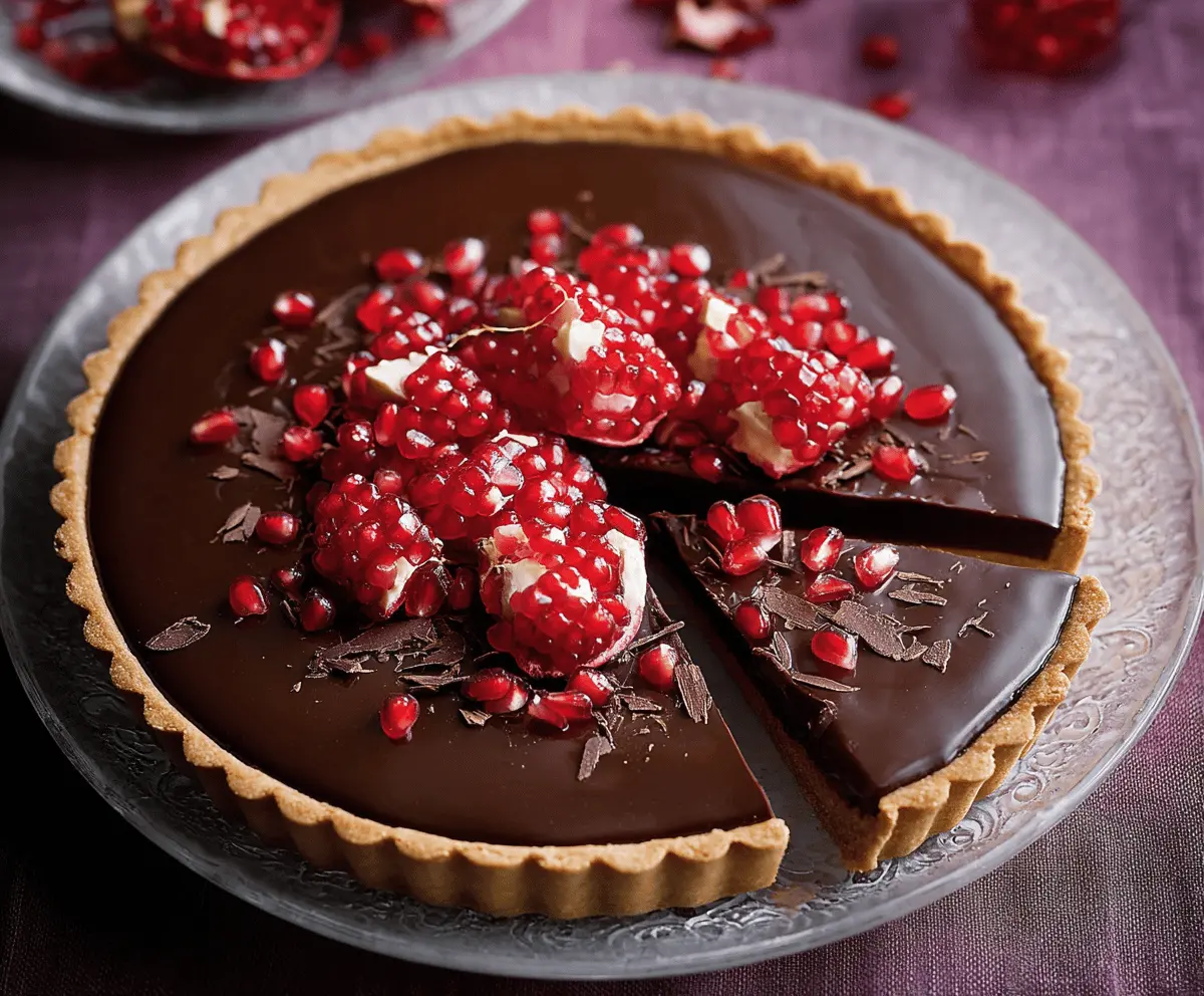 Delicious Chocolate Pomegranate Tart topped with fresh pomegranate seeds and rich chocolate ganache on a decorative plate.