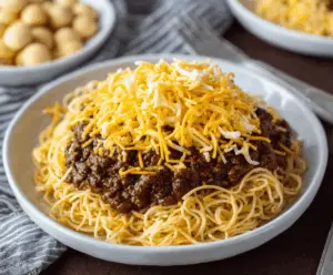 Delicious bowl of Cincinnati Chili served with noodles, topped with shredded cheese and onions, ready to enjoy.
