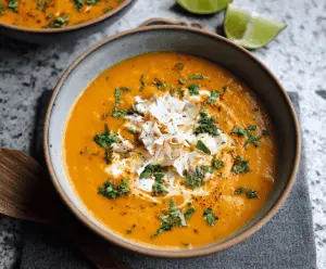 Creamy coconut curry sweet potato soup garnished with fresh herbs in a rustic bowl, showcasing vibrant orange color and smooth texture