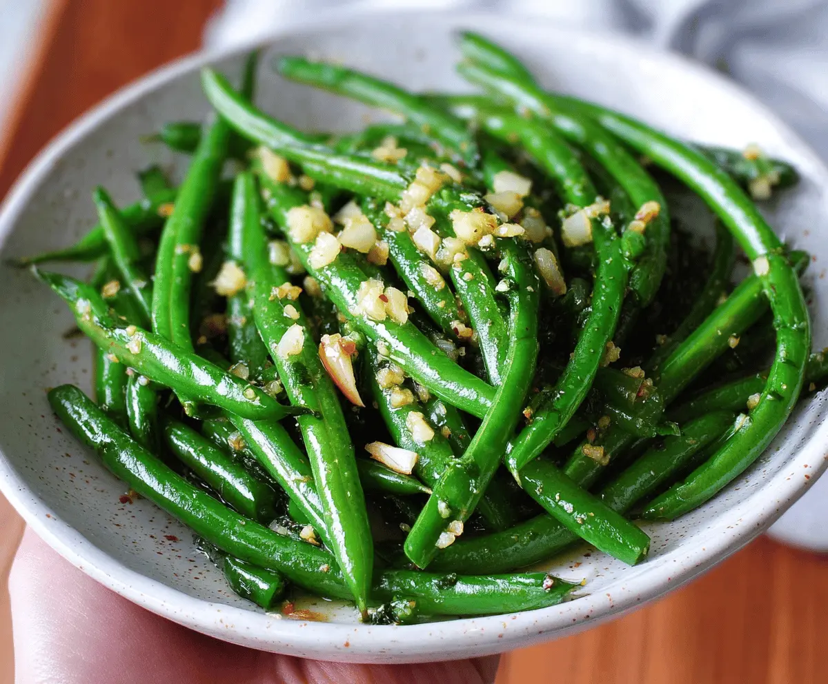 Delicious garlic butter green beans garnished with fresh herbs on a white plate.