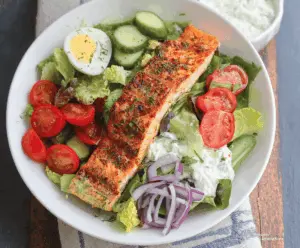 Fresh and healthy salmon salad with mixed greens, cherry tomatoes, cucumbers, and a lemon vinaigrette on a white plate