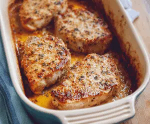 Juicy oven-baked pork chops served with roasted vegetables on a baking sheet, perfect for a hearty dinner.