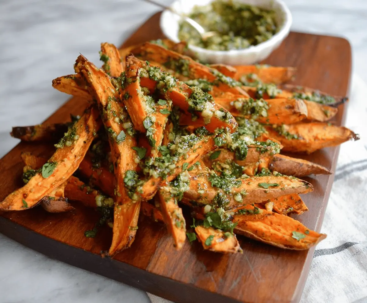 Crispy baked pesto sweet potato fries served with fresh herbs on a white plate, perfect for a healthy snack or appetizer