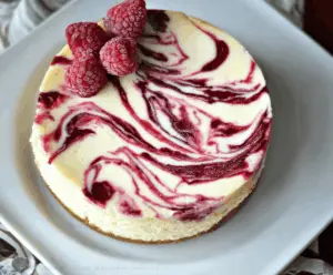 Creamy white chocolate raspberry swirl cheesecake garnished with fresh raspberries and a white chocolate drizzle.
