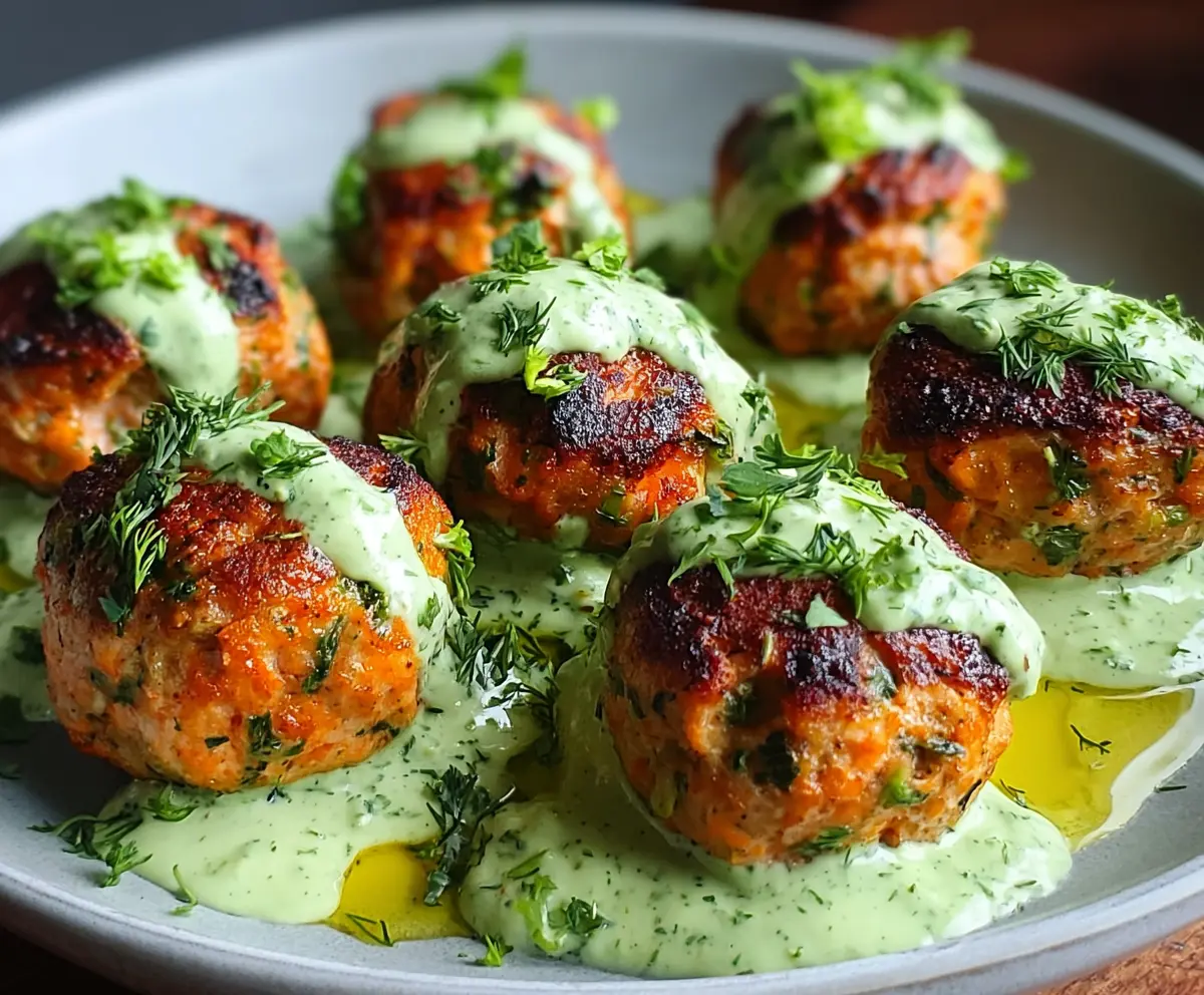 Delicious baked salmon meatballs served with a tangy avocado sauce on a white plate.