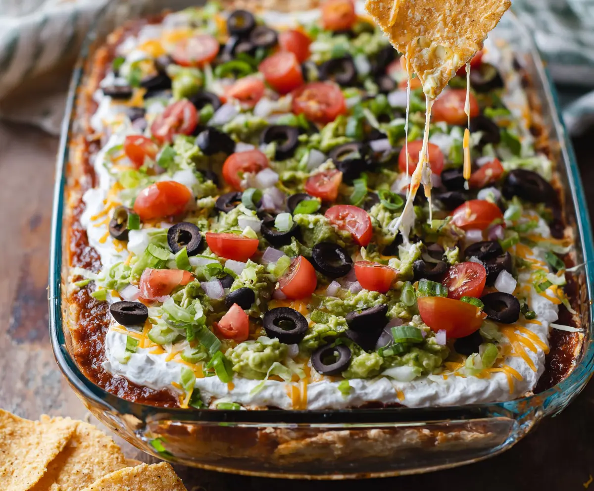 Colorful 7 Layer Bean Dip with layers of beans, cheese, and vegetables on a serving platter.