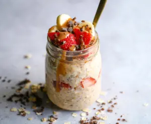 Delicious Banana Split Overnight Oats topped with fresh strawberries, bananas, and a dollop of whipped cream in a glass jar.