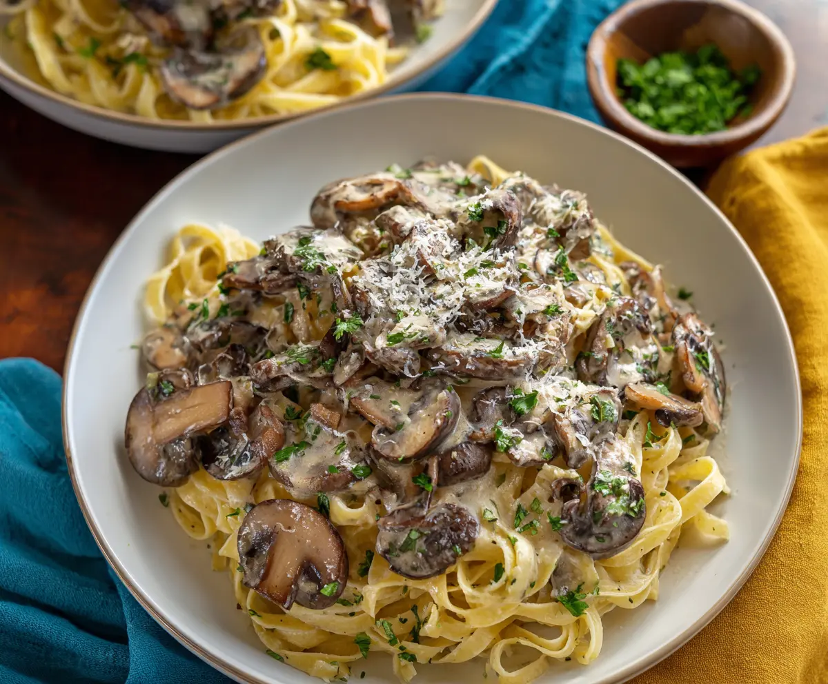 Delicious mushroom pasta with creamy sauce and fresh herbs on a white plate.