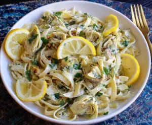 Creamy lemon artichoke pasta served with fresh herbs on a white plate.