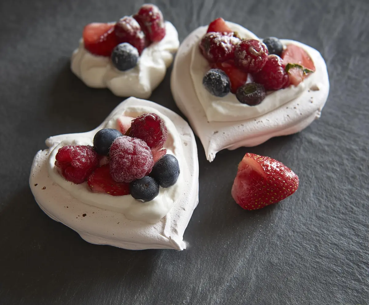Delicious mini heart-shaped Pavlovas topped with fresh berries and whipped cream