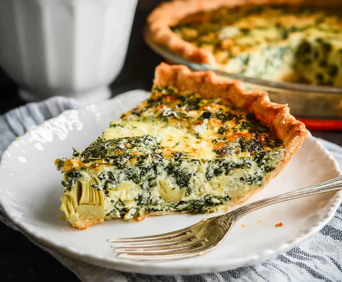 Delicious spinach and artichoke quiche garnished with fresh herbs, served as a savory breakfast or brunch dish.
