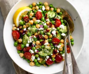 Fresh Mediterranean Pea Salad with feta cheese, cherry tomatoes, and herbs on a rustic wooden table.