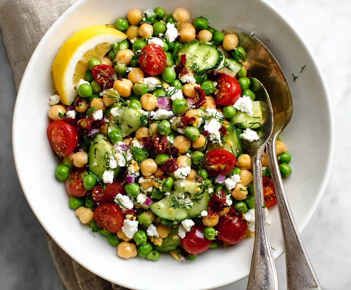 Fresh Mediterranean Pea Salad with feta cheese, cherry tomatoes, and herbs on a rustic wooden table.