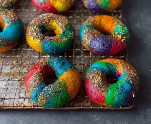 Colorful rainbow bagels with vibrant swirls and a creamy topping on a wooden platter.