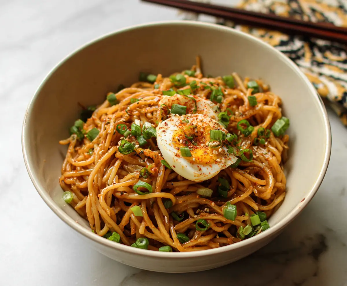 Bowl of savory Korean garlic noodles garnished with chopped scallions and sesame seeds.
